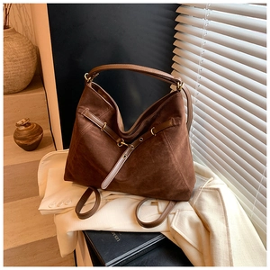 Close-up of dark brown suede tote bag with decorative leather straps and metallic buckles