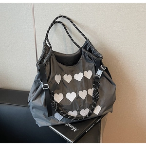 Detail of grey nylon tote bag with white heart patches and woven drawstring handles