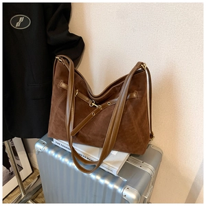 Deep brown matte suede tote bag with gold hardware placed on a silver suitcase