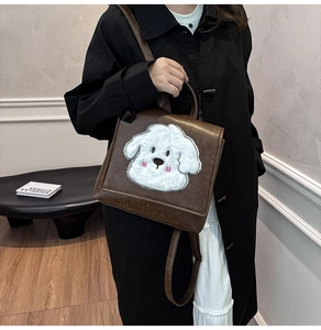 Detail of dark brown leather backpack featuring a white plush dog patch on the front flap
