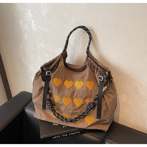 Detail of brown nylon tote bag featuring yellow heart embroidery and rope handle