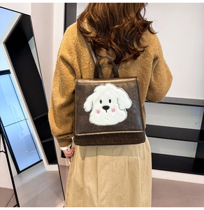 Detail of a brown faux leather backpack with plush puppy embroidery on a model