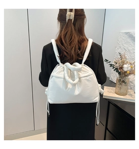 Rear view of a white padded drawstring backpack shown on a model in a minimalist room