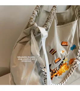 Detail der Katzenstickerei und des verstellbaren Schultergurts an khakifarbener Tote-Bag