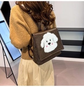 Close-up of a brown leather backpack with a plush puppy charm on a model in autumn outfit