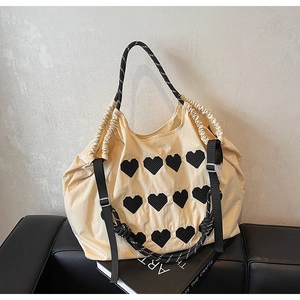 Detail of beige tote bag featuring heart embroidery and woven handles on a sofa