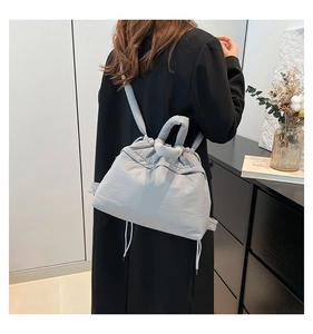 Light grey quilted backpack with padded handle and drawstring closure on black wool coat