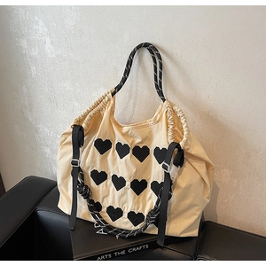 Close-up of cream canvas hobo bag featuring nine black heart mesh appliques on leather sofa