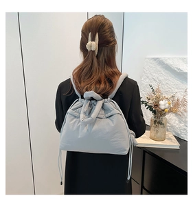 Back view of light grey-blue quilted puffer backpack with drawstring closure on model