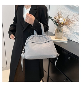 Light gray pleated nylon tote bag with drawstring detail shown on a business casual model