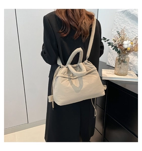 Quilted beige padded nylon bag shown on shoulder of model in a sleek black suit outfit