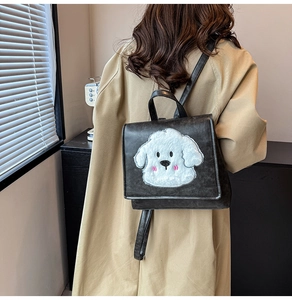 Detail showing plush cartoon puppy patch on premium black leather mini backpack