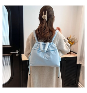 Back view of model wearing a light blue quilted down backpack with drawstring detail