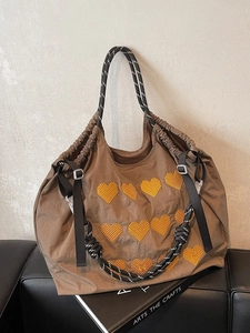 Brown tote bag with heart embroidery and rope handles on a black leather bench