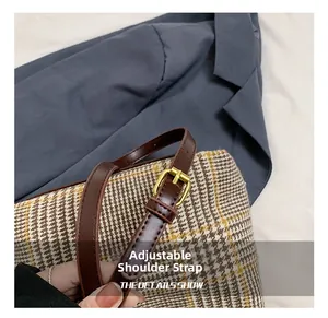 Detail of adjustable dark brown leather shoulder strap and gold buckle on a plaid bag