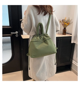 Rear view of a model wearing the green padded nylon drawstring backpack with top handle