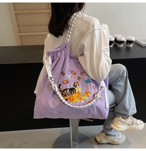 Detail der süßen Katzenstickerei und des Kordelriemens an einer lila Stofftasche