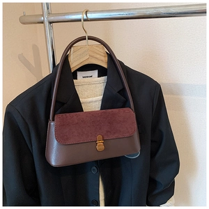 Detail of vintage burgundy suede flap bag with gold buckle on a stylish clothing rack