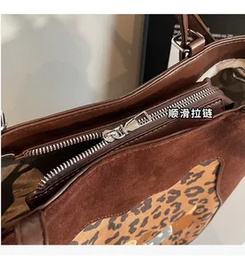 Detailed close-up of smooth silver zipper and leopard print trim on brown suede tote bag