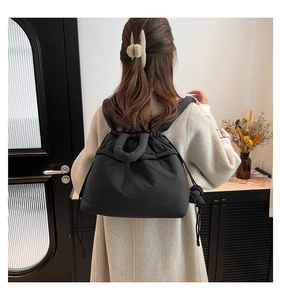 Back view of model wearing a black quilted drawstring tote bag in a minimalist room