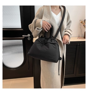 Detail of black puffy nylon drawstring tote bag worn crossbody in minimalist setting