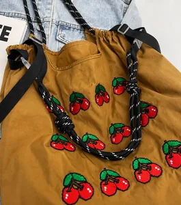 Detailed close-up of cherry embroidery and woven adjustable strap on the brown tote bag