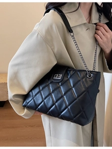 Sac cabas noir matelassé avec bandoulière chaîne porté sur un trench-coat beige élégant