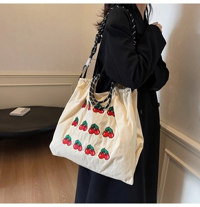 Detail van de crèmekleurige canvas tas met kersenborduursel en handgrepen van touw