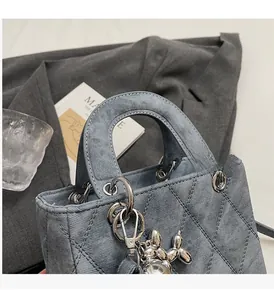 Close-up of gray quilted denim handbag featuring silver metal rings and a balloon dog charm