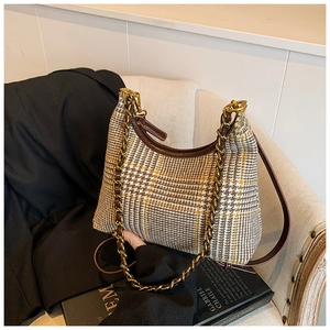 Detail of checkered tweed shoulder bag with golden chain strap on a soft beige fabric sofa