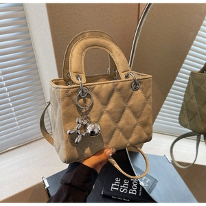 Detail view of beige quilted leather handbag featuring metal handles and a dog charm