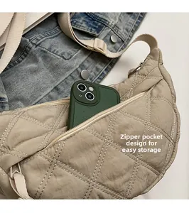 Detail view of beige quilted crescent bag featuring a zippered front pocket for phone storage