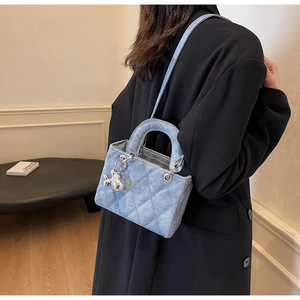 Detail view of light blue denim quilted handbag with silver rabbit charm and metallic links