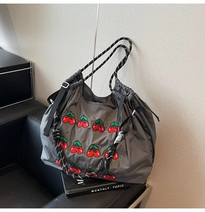 Detail van grijze nylon draagtas met kersenborduurwerk en gevlochten touwgrepen