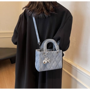 Detail of light blue quilted denim bag with silver balloon dog charm and top handles