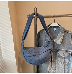 Close-up of blue quilted crescent shoulder bag with diamond stitching on metal hanger