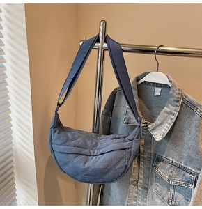 Close-up of blue quilted half-moon bag with adjustable strap on a metal hanger