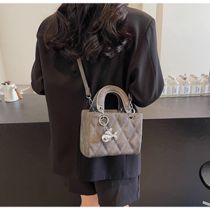 Detail of dark grey quilted handbag with silver balloon dog charm worn by a model