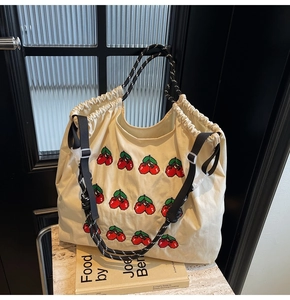 Detail van beige canvas tas met geborduurde kersen en zwart geweven touw handvat