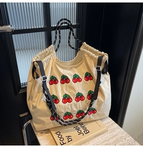 Detail van crème tote bag met kersenborduurwerk, geweven handgrepen en trekkoord