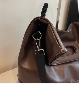 Detail of glossy dark brown tote bag showing silver metal buckles and woven nylon strap