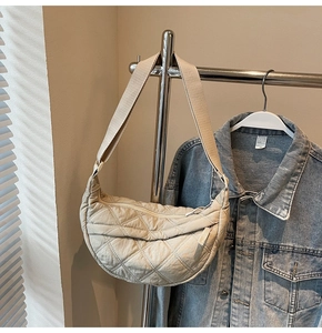 Detail of beige quilted crescent bag with diamond stitch texture and fabric zipper pull