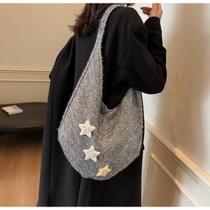 Detail der grauen Stricktasche mit drei bunten Stoffstern-Anhängern auf schwarzem Mantel