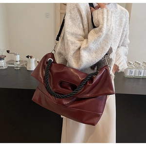 Detailed close-up of wine red PU leather tote with black knot woven handle on a coffee table