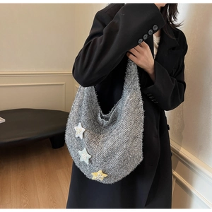 Detail der grauen Tweed-Stricktasche mit bunten Sternen auf einem schwarzen Blazer