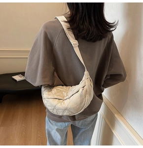 Detail of cream quilted crescent bag showing textured nylon fabric and adjustable strap