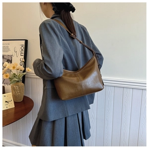 Brown semi-circle hobo bag worn as an underarm shoulder bag with adjustable strap