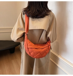 Detail of orange quilted crescent bag featuring adjustable strap and diamond stitching