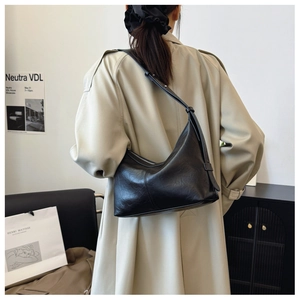 Model wearing a black crescent shoulder bag with matte leather texture and silver buckle