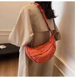 Detail of orange quilted crescent bag featuring adjustable strap and padded nylon texture